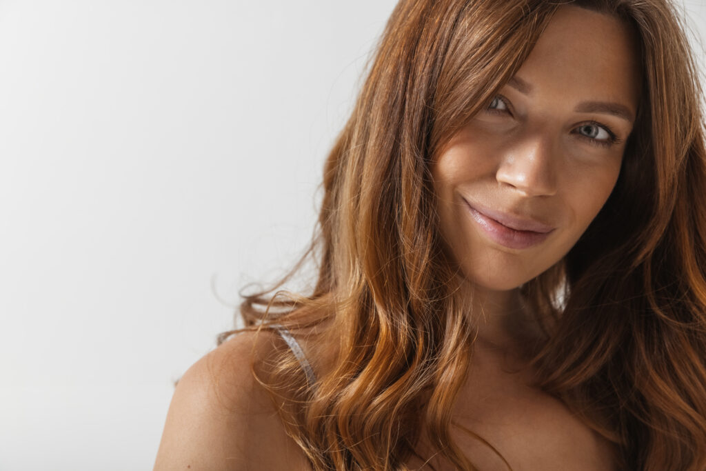 Close-up portrait of young beautiful red-headed woman without makeup isolated over light studio background. Natural beauty concept.